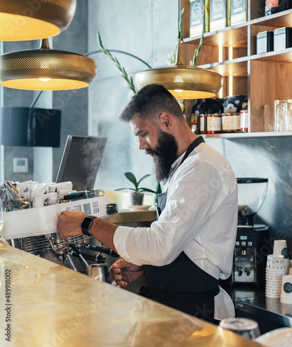 Handsome barista with beard preparing cappuccino on steam espresso coffee machine in the cafe