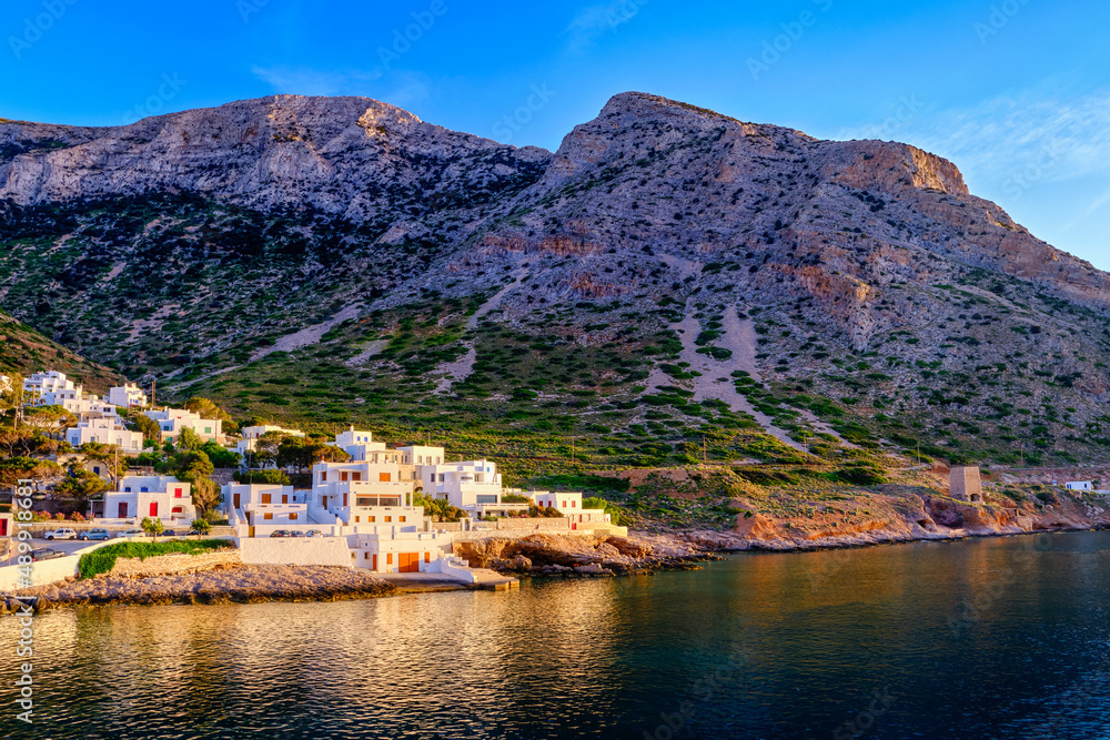 Beautiful view of Mediterranean island at sunset. Small Greek fisherman village in rays of low sun. Sun flares, whitewashed houses, Milos, Greece.