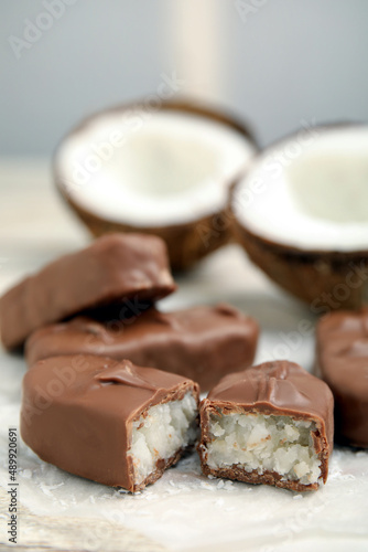 Delicious milk chocolate candy bars with coconut filling on white table, closeup