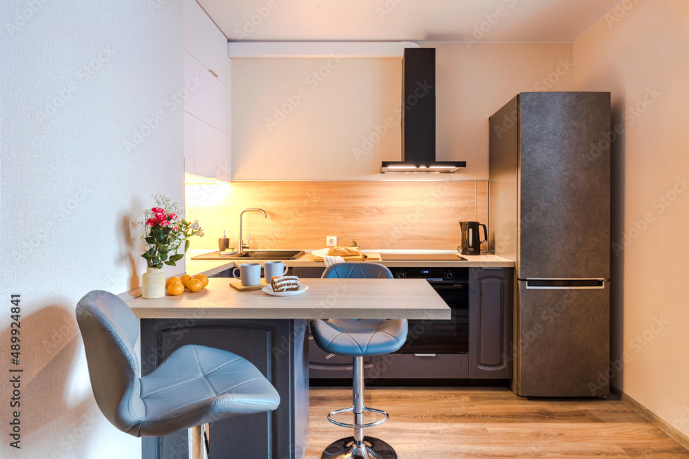 Minimalist wooden grey kitchen with handleless facades and bar table, smart storage system. Kitchen room organization Minimalist wooden grey kitchen with handleless facades and bar table, smart storage system. Kitchen room organization