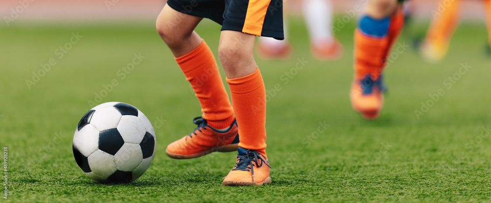 Fototapeta premium Closeup image of young football player kicking ball. School kids play sports outdoor