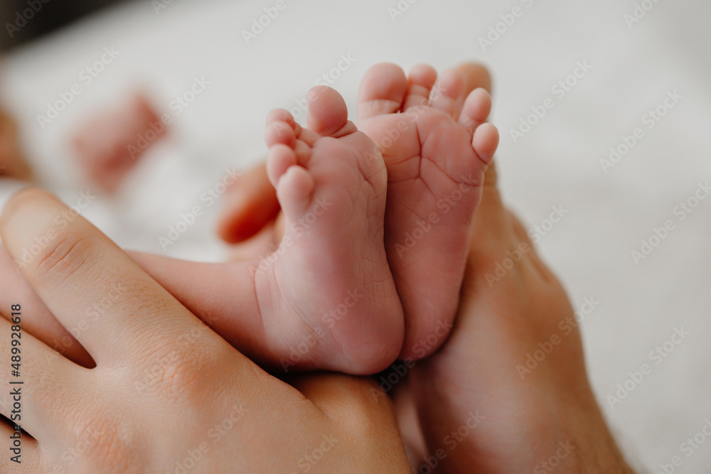 Feet of a newborn baby in the hands of parents. Happy Family oncept. Mum and Dad hug their baby's legs. Feet of a newborn baby in the hands of parents. Happy Family oncept. Mum and Dad hug their baby's legs.