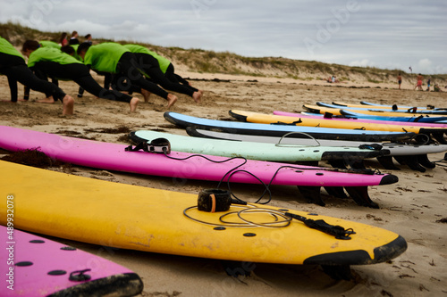 Students from a surf school warm up their muscles on the sand of the beach before starting class. In the foreground is a colored board washed up on the beach. photo