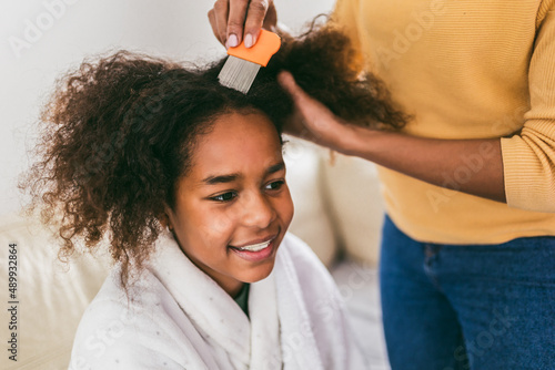 Mother doing head lice cleaning on her daughter curly hair.