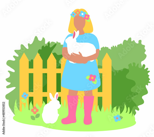 The girl is holding a white bunny in her arms. Fence, bushes in the background. Green grass spring landscape. Rabbit farm. Fluffy pets.