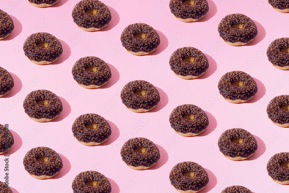 Fototapeta premium Arranged ring donuts whith chocolate glaze and small brown crumbs on a pink pastel background. Minimal concept and design. Pattern.