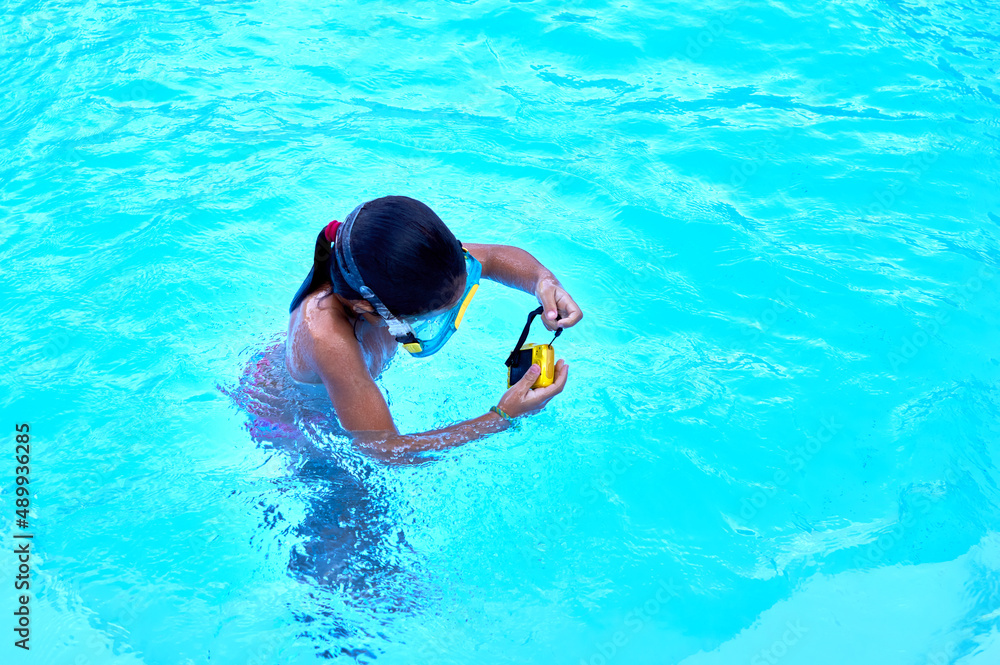 6-8 year old girl with diving goggles and an adventure camera plays in a pool.