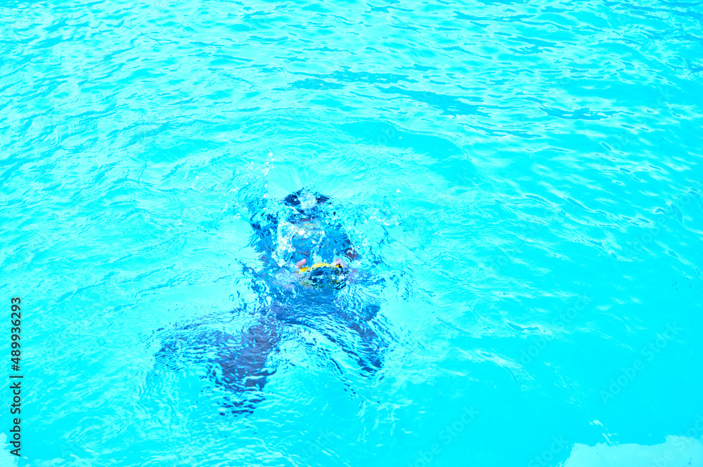 person splashing under the blue water of an open-air pool 