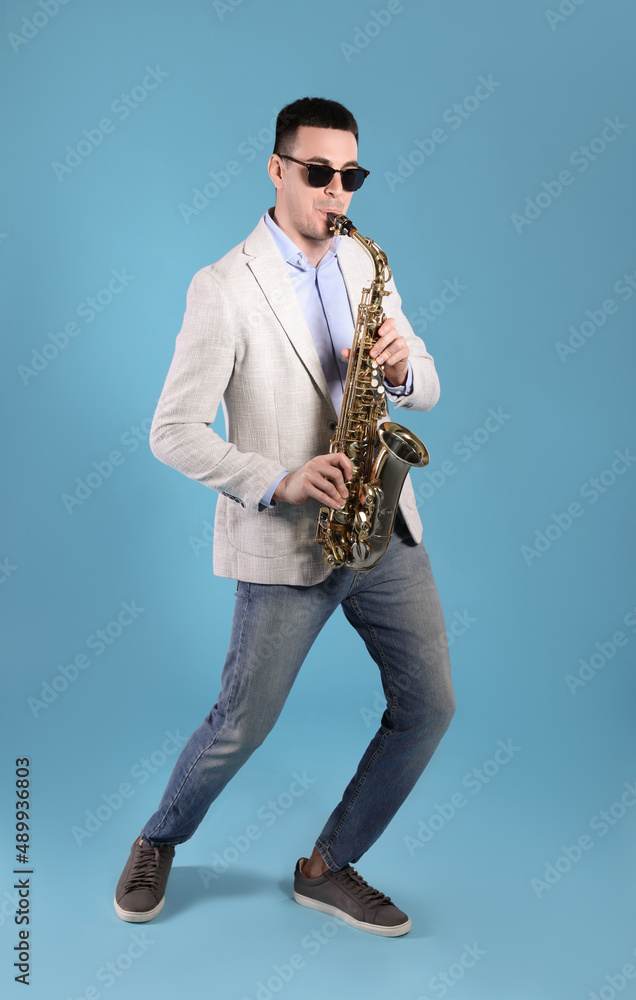 Fototapeta premium Young man playing saxophone on light blue background