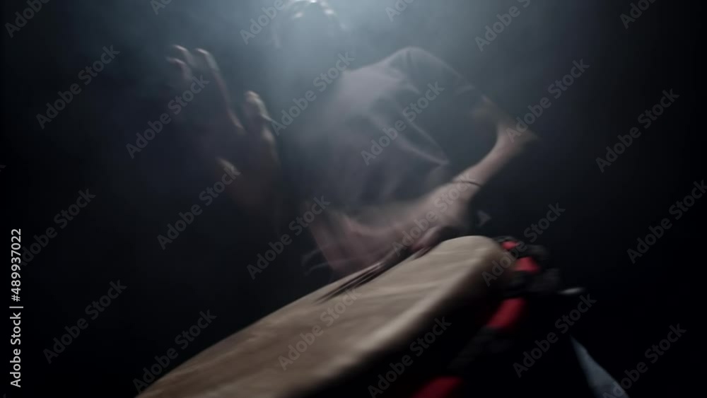 African American man plays an African folk musical instrument, bongo drum, in dark studio filled with smoke, front view, bottom view. Concept of music and performance African American man plays an African folk musical instrument, bongo drum, in dark studio filled with smoke, front view, bottom view. Concept of music and performance