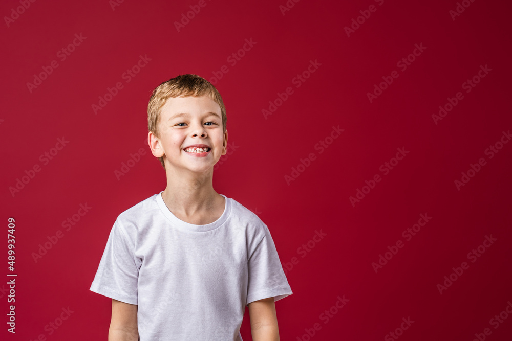 Portrait of a happy little boy of 7 years old, smiling sweetly, standing on a red background in the studio. The child is positive and looks confidently at the camera. Advertising Portrait of a happy little boy of 7 years old, smiling sweetly, standing on a red background in the studio. The child is positive and looks confidently at the camera. Advertising