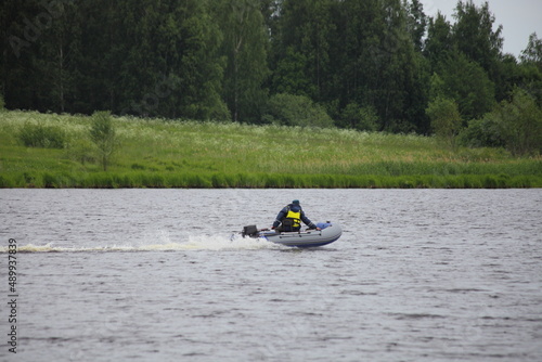 Small inflatable boat floating on European river on green forest on far shore background at summer day. Active outdoor recreation on the water.