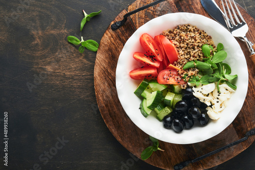 Vegetarian Vegan salad bowl or buddha bowl with tomato, cucumber, mozzarella cheese, quinoa, olives and microgreens. Healthy and balanced food concept on old wooden dark background Top view copy space