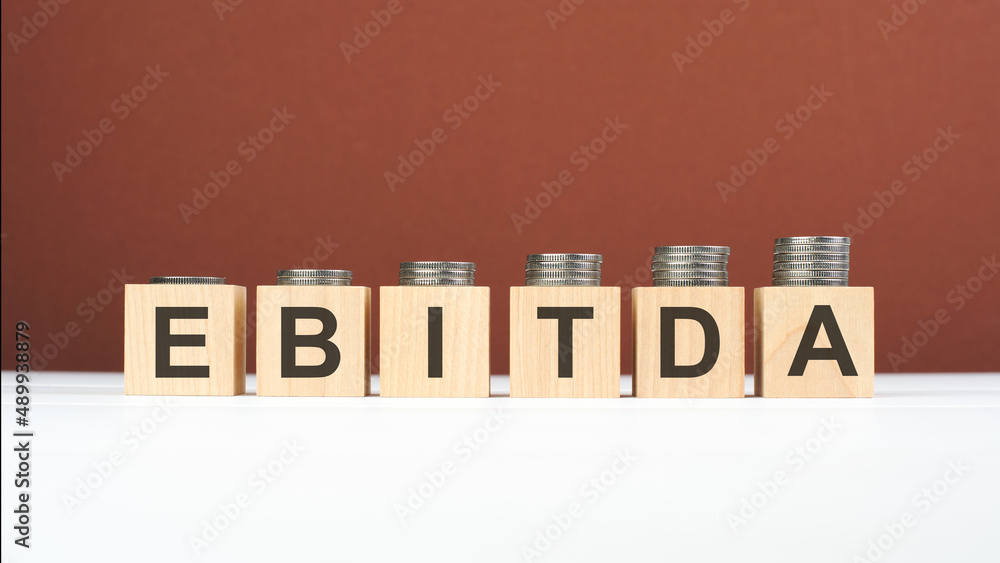 Obraz premium EBITDA text on wooden blocks with coins on brown background