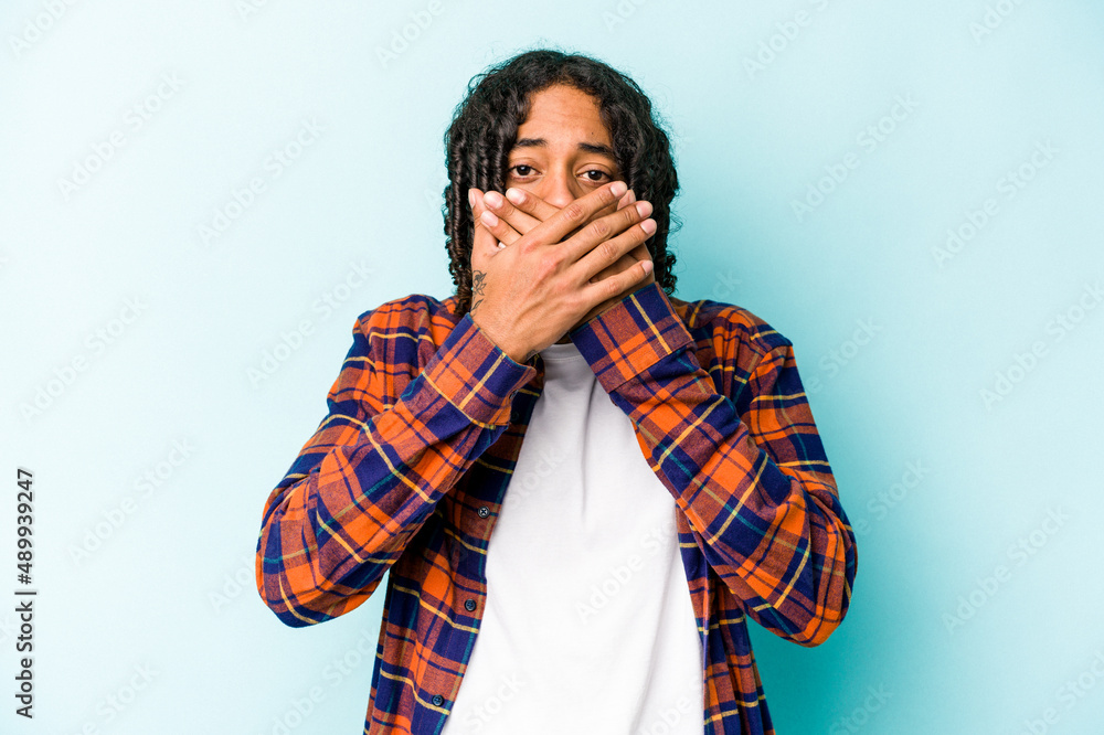 Young African American man isolated on blue background covering mouth with hands looking worried. Young African American man isolated on blue background covering mouth with hands looking worried.