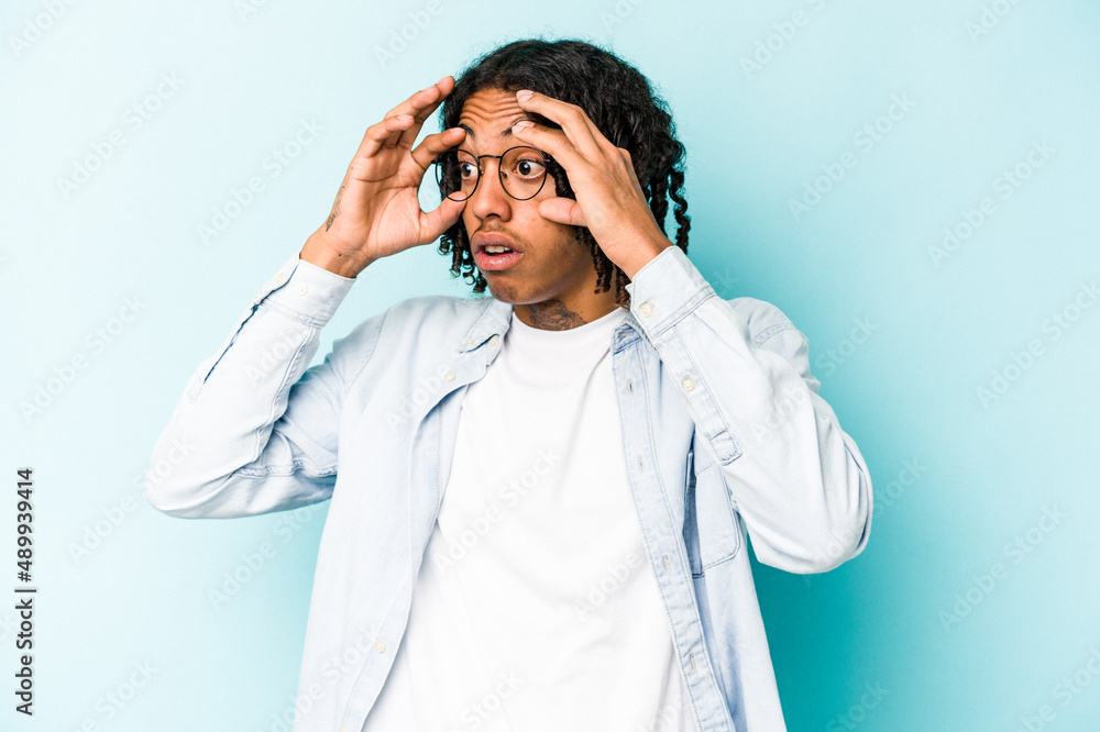 Young African American man isolated on blue background keeping eyes opened to find a success opportunity. Young African American man isolated on blue background keeping eyes opened to find a success opportunity.