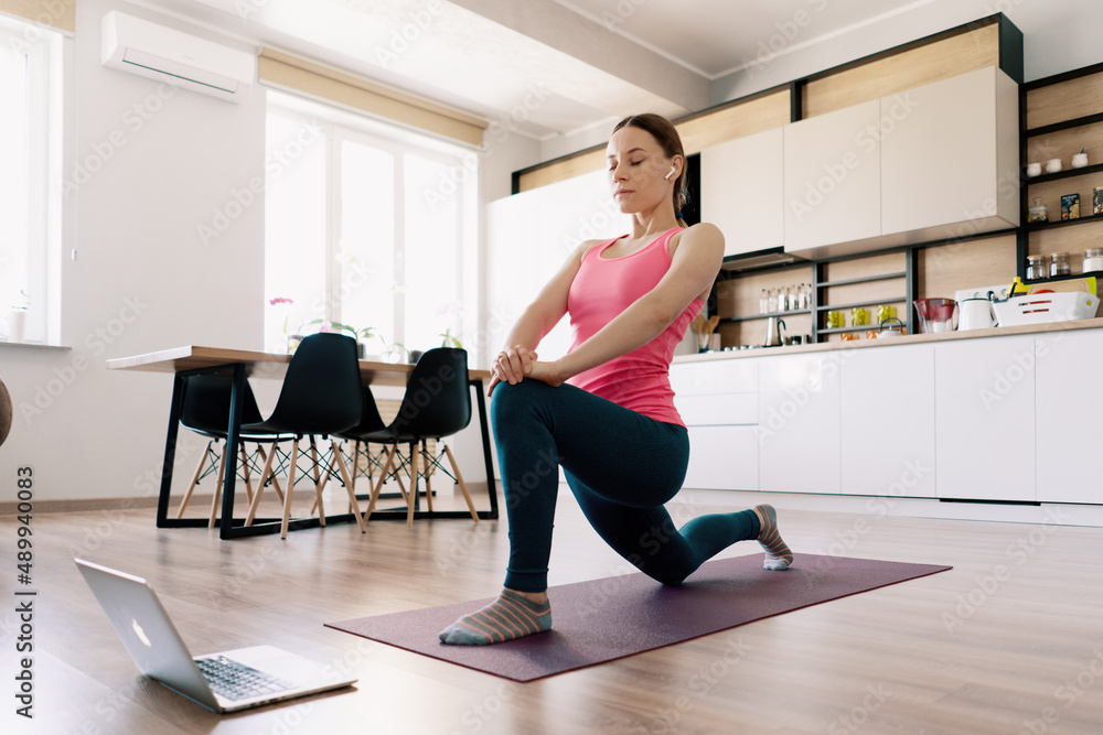 Attractive woman practicing yoga at home using online training instructions Attractive woman practicing yoga at home using online training instructions