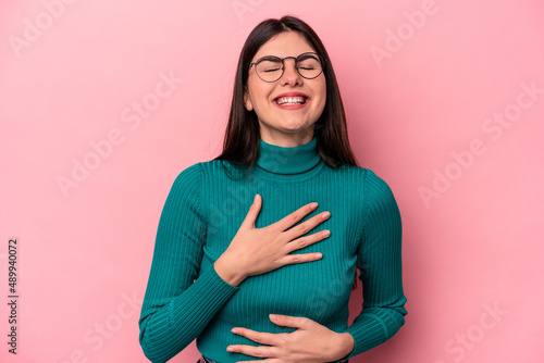 Young caucasian woman isolated on pink background laughs happily and has fun keeping hands on stomach.