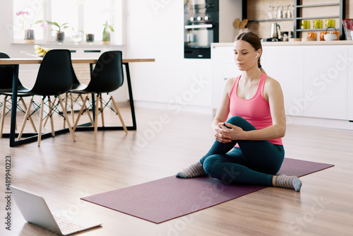 Attractive woman practicing yoga at home using online training instructions