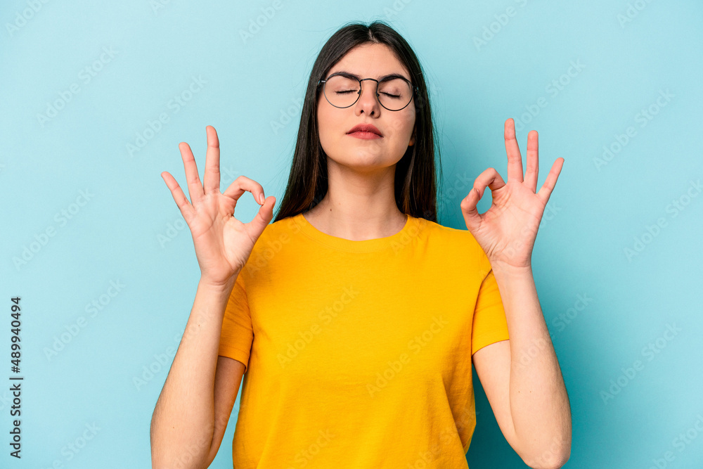Young caucasian woman isolated on blue background relaxes after hard working day, she is performing yoga. Young caucasian woman isolated on blue background relaxes after hard working day, she is performing yoga.