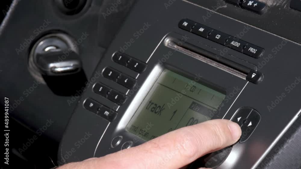 The hand of a man inserts a CD into the car radio. Playing track 1. Using the rotating knob increases the volume. Car stereo. Inside car video. Audio CD.
The hand of a man inserts a CD into the car radio. Playing track 1. Using the rotating knob increases the volume. Car stereo. Inside car video. Audio CD.