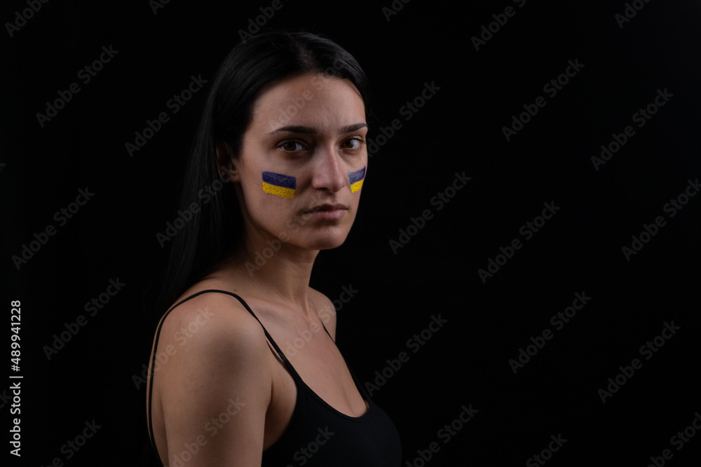 Portrait of serious ukrainian woman with blue and yellow ukrainian flag on her cheek.The symbol of the inviolability of the Ukrainian people. Dark background. Space for your text Portrait of serious ukrainian woman with blue and yellow ukrainian flag on her cheek.The symbol of the inviolability of the Ukrainian people. Dark background. Space for your text