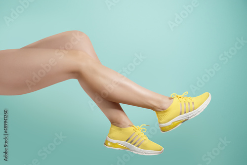 Studio shot of a young woman's legs in a pair of yellow sport shoes for running on turquoise background