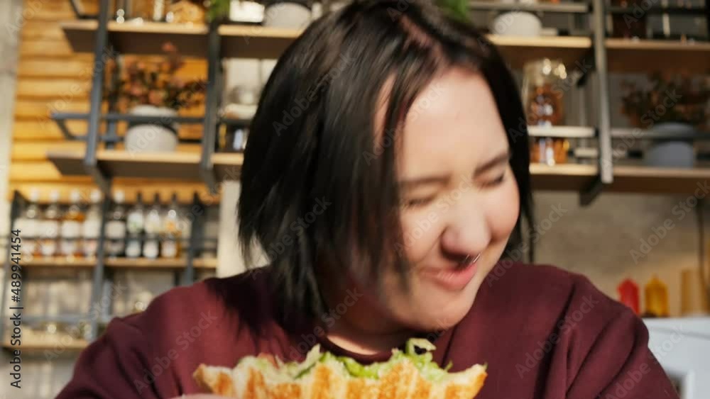 Portrait. A plump cheerful girl with a metal ring in her nose chews a sandwich and laughs in a fast food restaurant. slow motion Portrait. A plump cheerful girl with a metal ring in her nose chews a sandwich and laughs in a fast food restaurant. slow motion