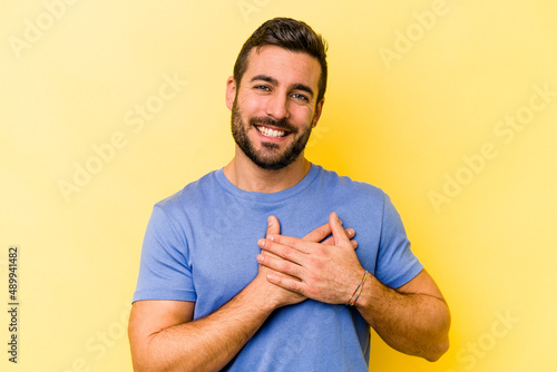 Young caucasian man isolated on yellow background has friendly expression, pressing palm to chest. Love concept.