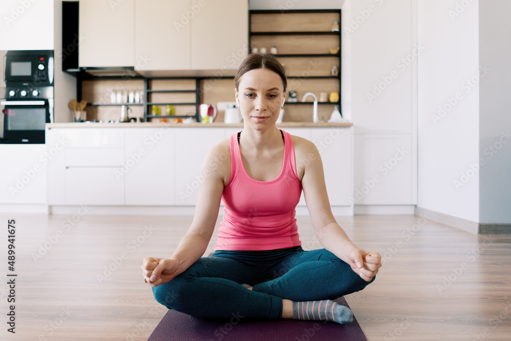 Fototapeta premium Attractive woman practicing yoga at home in lotus pose
