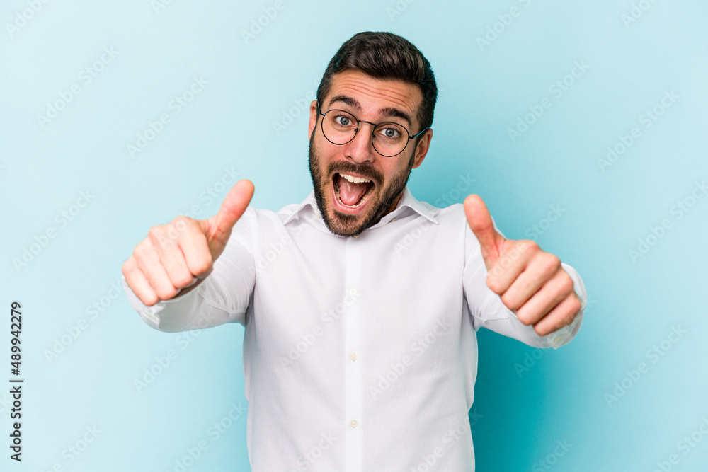 Young caucasian man isolated on blue background raising both thumbs up, smiling and confident. Young caucasian man isolated on blue background raising both thumbs up, smiling and confident.