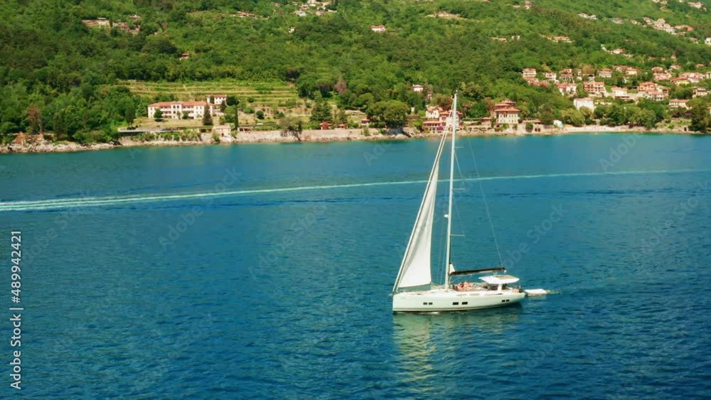 Sailboat sails against big forestry island with small houses in summer. Yacht reflecting on blue water of Adriatic sea on sunny day. Aerial view Sailboat sails against big forestry island with small houses in summer. Yacht reflecting on blue water of Adriatic sea on sunny day. Aerial view