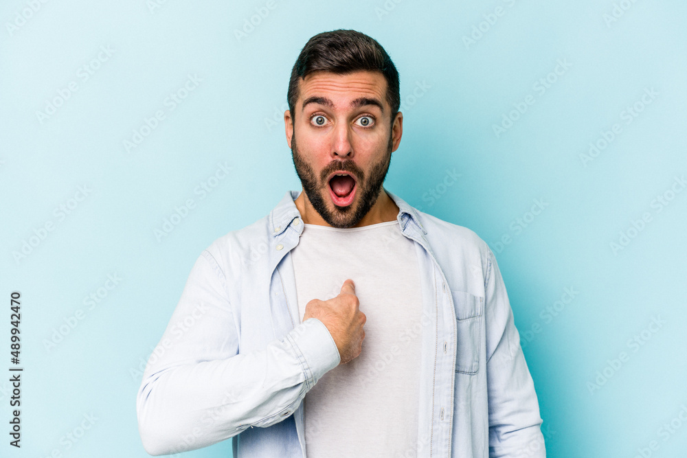 Young caucasian man isolated on blue background surprised pointing with finger, smiling broadly. Young caucasian man isolated on blue background surprised pointing with finger, smiling broadly.