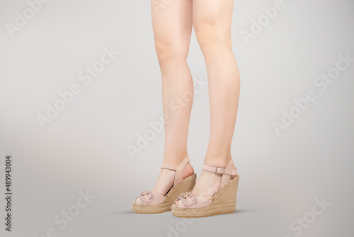Studio shot of a young woman's legs in a pair of pink platform wedge shoes on grey background