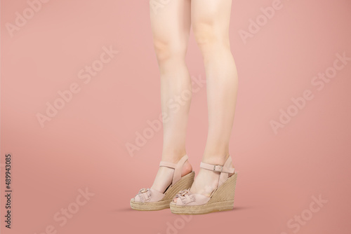 Studio shot of a young woman's legs in a pair of pink platform wedge shoes on pink background
