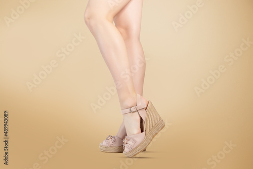 .Studio shot of a young woman's legs in a pair of pink platform wedge shoes on golden background