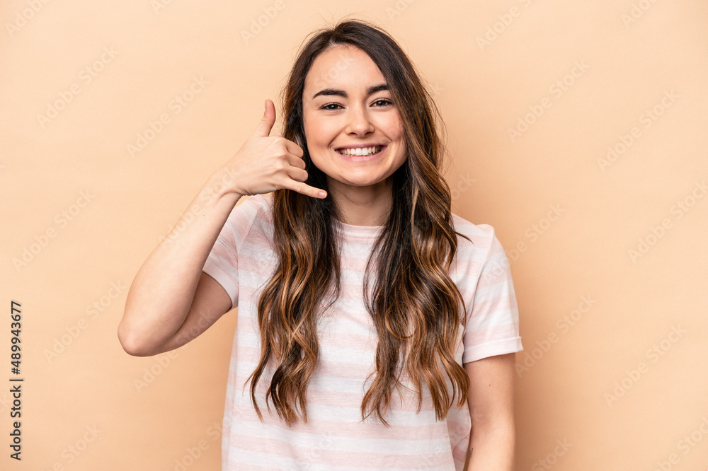 Young caucasian woman isolated on beige background showing a mobile phone call gesture with fingers. Young caucasian woman isolated on beige background showing a mobile phone call gesture with fingers.