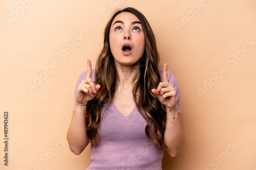Young caucasian woman isolated on beige background pointing upside with opened mouth.