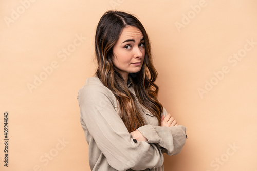 Young caucasian woman isolated on beige background suspicious, uncertain, examining you. © Asier