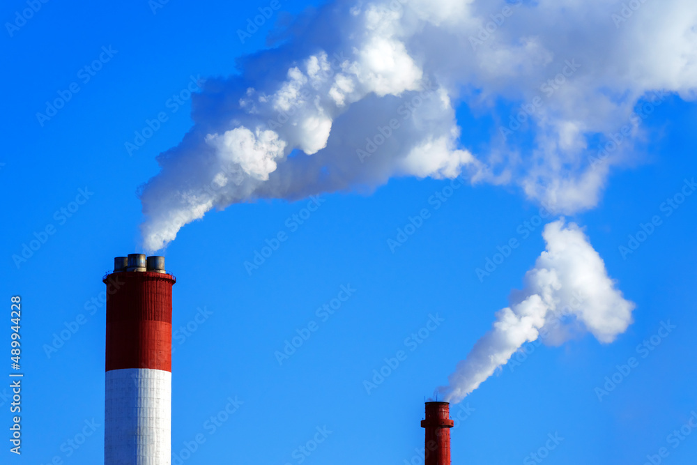 Two red-white pipes with smoke against the background of a blue sky Two red-white pipes with smoke against the background of a blue sky