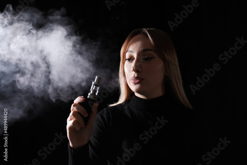Young woman using electronic cigarette on black background
