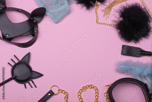 Set of erotic toys for BDSM. The game of sexual slavery with a whip, handcuffs and leather mask on a light pink background.