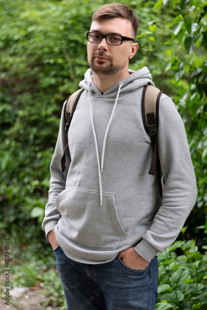 Young brunette man in glasses stands on the street outside in spring against the of green trees