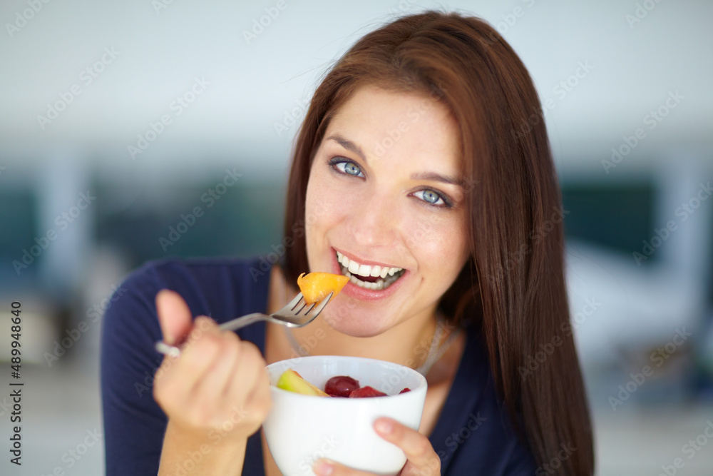 Indulging in a tasty, healthy snack. Portrait of a smiling young woman eating a healthy fruit salad for lunch. Indulging in a tasty, healthy snack. Portrait of a smiling young woman eating a healthy fruit salad for lunch.