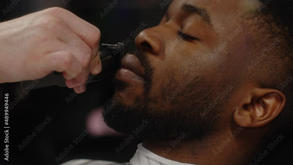 A white-skinned guy straightens the line of his mustache to a young African-American guy A white-skinned guy straightens the line of his mustache to a young African-American guy