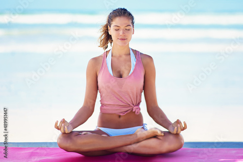 Shes one with nature. Shot of a young woman doing yoga at the beach.