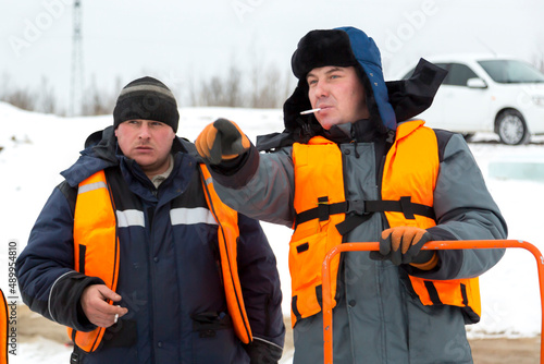 Portrait of fitters in orange color vests on the ice of the lake with cigarettes