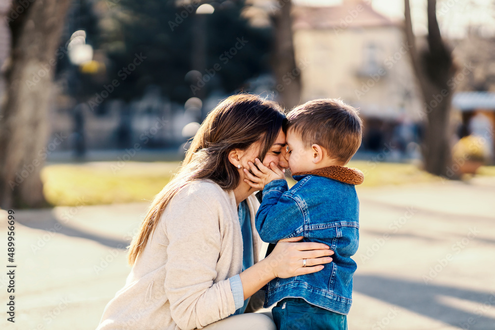 Fototapeta premium A little boy kissing his mommy while she hugging him in a park.
