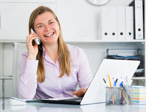 Smiling woman worker talking on phone while working in office © JackF
