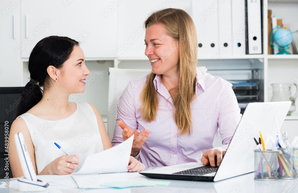 Fototapeta premium Two smiling women workers working effectively on project in office